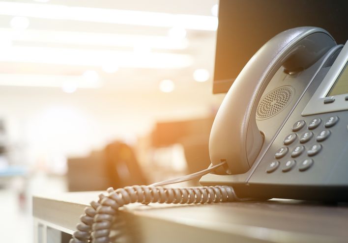 A VoIP phone sitting on the edge of the of a table in warm lighting.